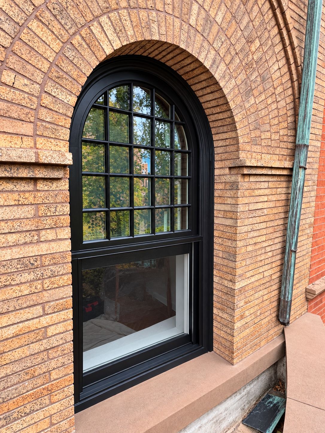 Close view of an arched top double hung window with a black frame and divided lites in the upper sash, set in a brick arch