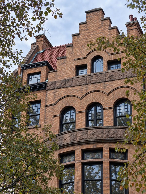 Finished third and fourth floor windows on the front facade, with black frames, arched heads and divided lites, framed by tree branches