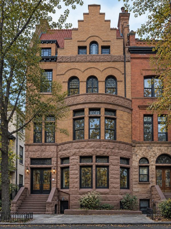 Front facade of the building in autumn light, a brick and brownstone row house with a stepped gable and black framed windows