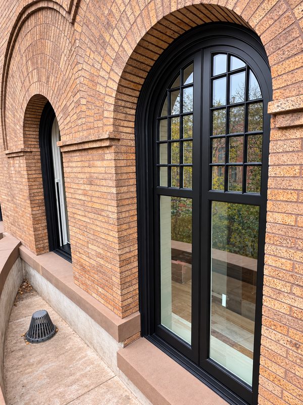 Close view of a tall arched window with a black frame set in a brick arch, with a smaller arched window beside it