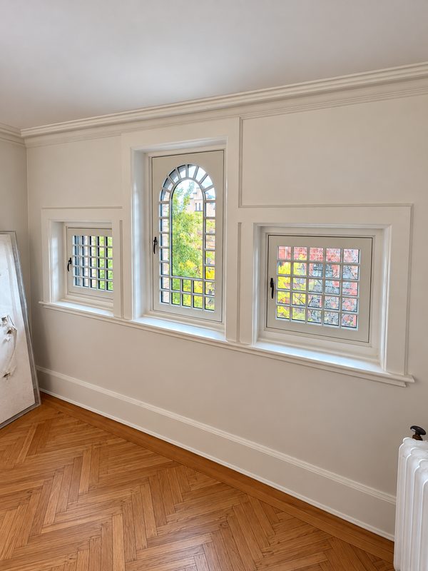 Interior wall with a tall arched window between two smaller divided lite windows, all with white frames, above a herringbone wood floor
