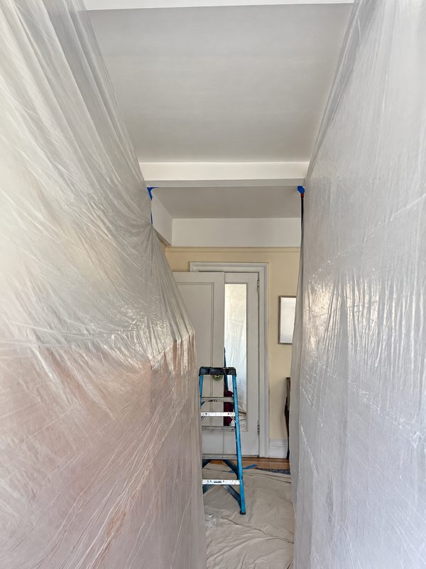 Passage lined with plastic sheeting leading to a room, with a ladder at the far end