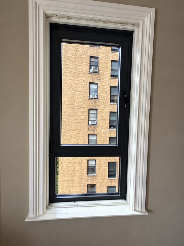 New black framed window with white casing, looking out at a tan brick building