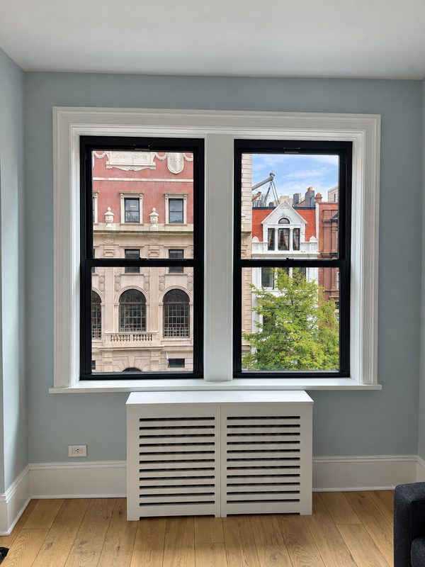Two new black framed double hung windows with white casing above a white radiator cover in a light blue room