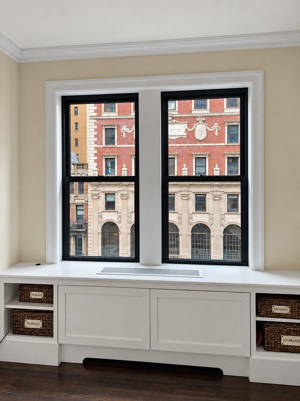 Two new black framed double hung windows above a built in window seat with storage