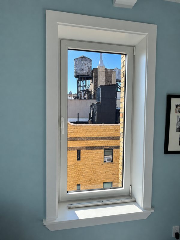 New white framed window with white casing in a light blue room, with a rooftop water tank in view