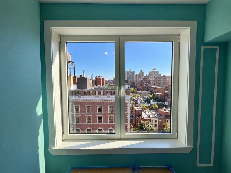 New white framed window in a teal alcove with a view of the skyline and a brick building