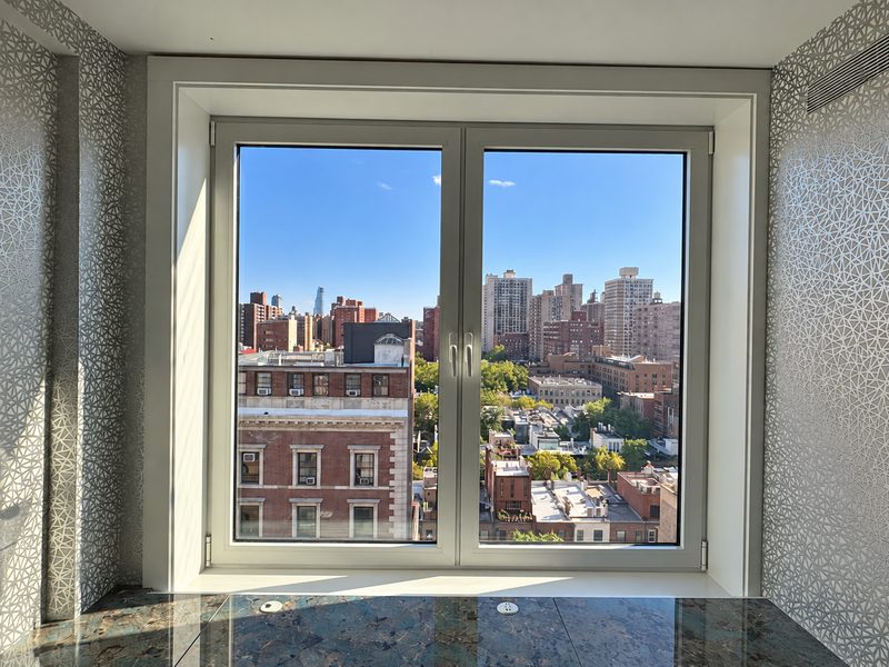 Wide new white framed window with a view of the skyline, set between patterned walls above a stone counter