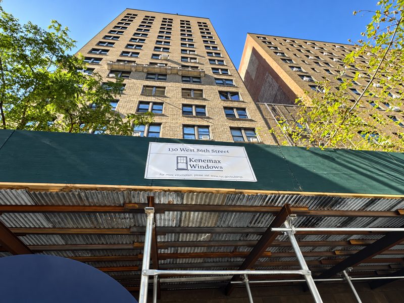Looking up at the building from under the sidewalk shed, with a project banner reading 130 West 86th Street Kenemax Windows