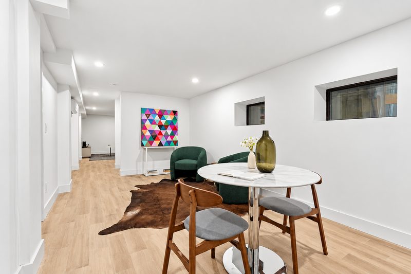 Dining area with a round table, two small black framed windows set high in the wall and a long hallway beyond