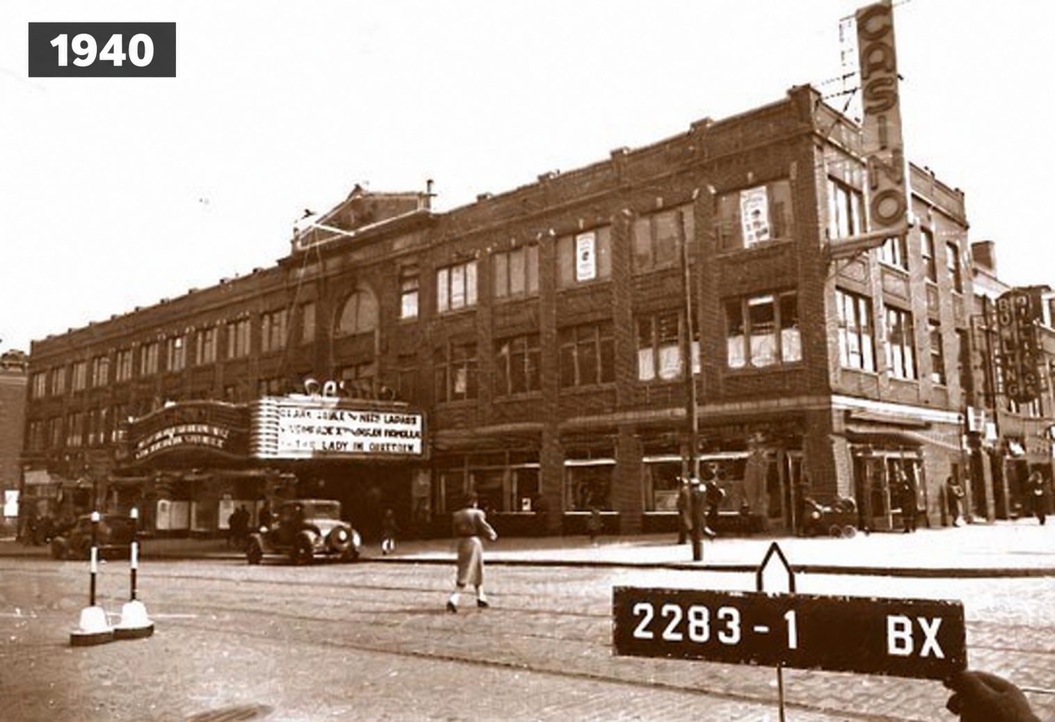Restored archival view of the theatre building at the corner, labeled 1940, with its marquee, a tall vertical sign reading Casino, an early car and a numbered placard in the foreground