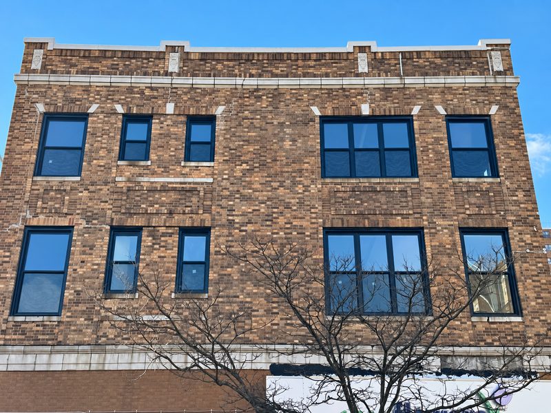 Close view of new dark framed windows in the brick facade, with stone trim and bare tree branches in front