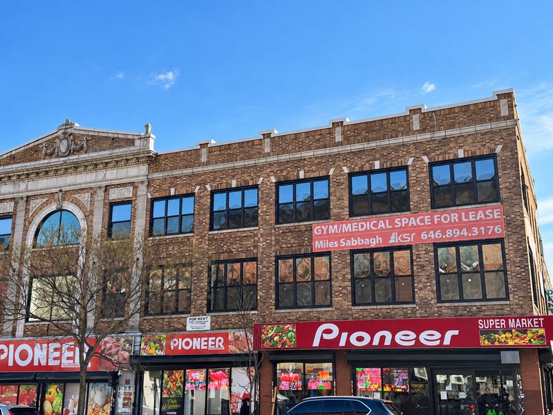 Upper floors with new dark framed windows beside the decorative pediment, above a supermarket sign