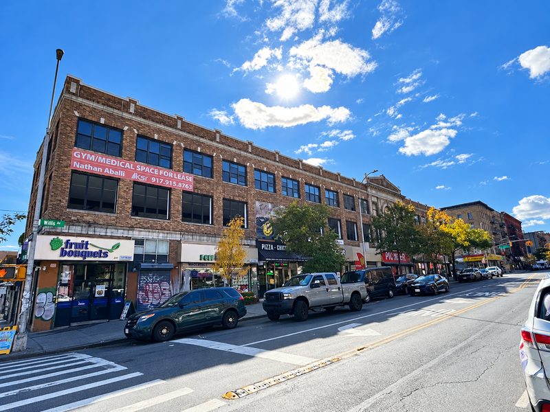 View along the long brick building from across the street, with new dark framed windows on the upper floors and parked cars at the curb
