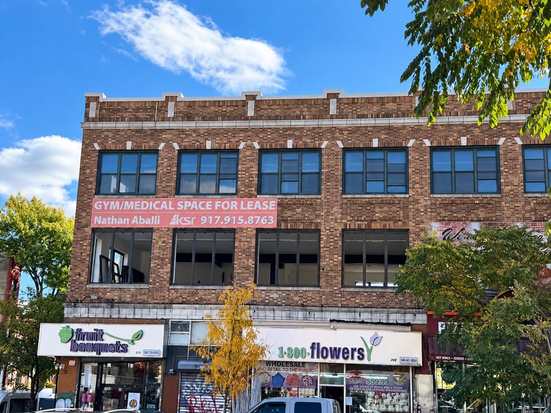 Brick facade above a flower shop and a fruit shop, with rows of new dark framed windows and autumn trees