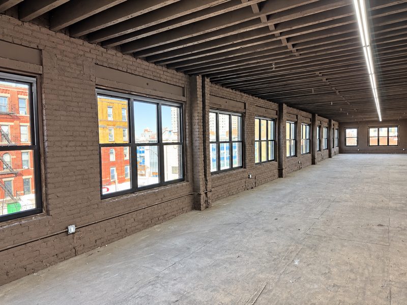 Open upper floor with exposed ceiling joists, painted brick walls and a long run of new dark framed windows