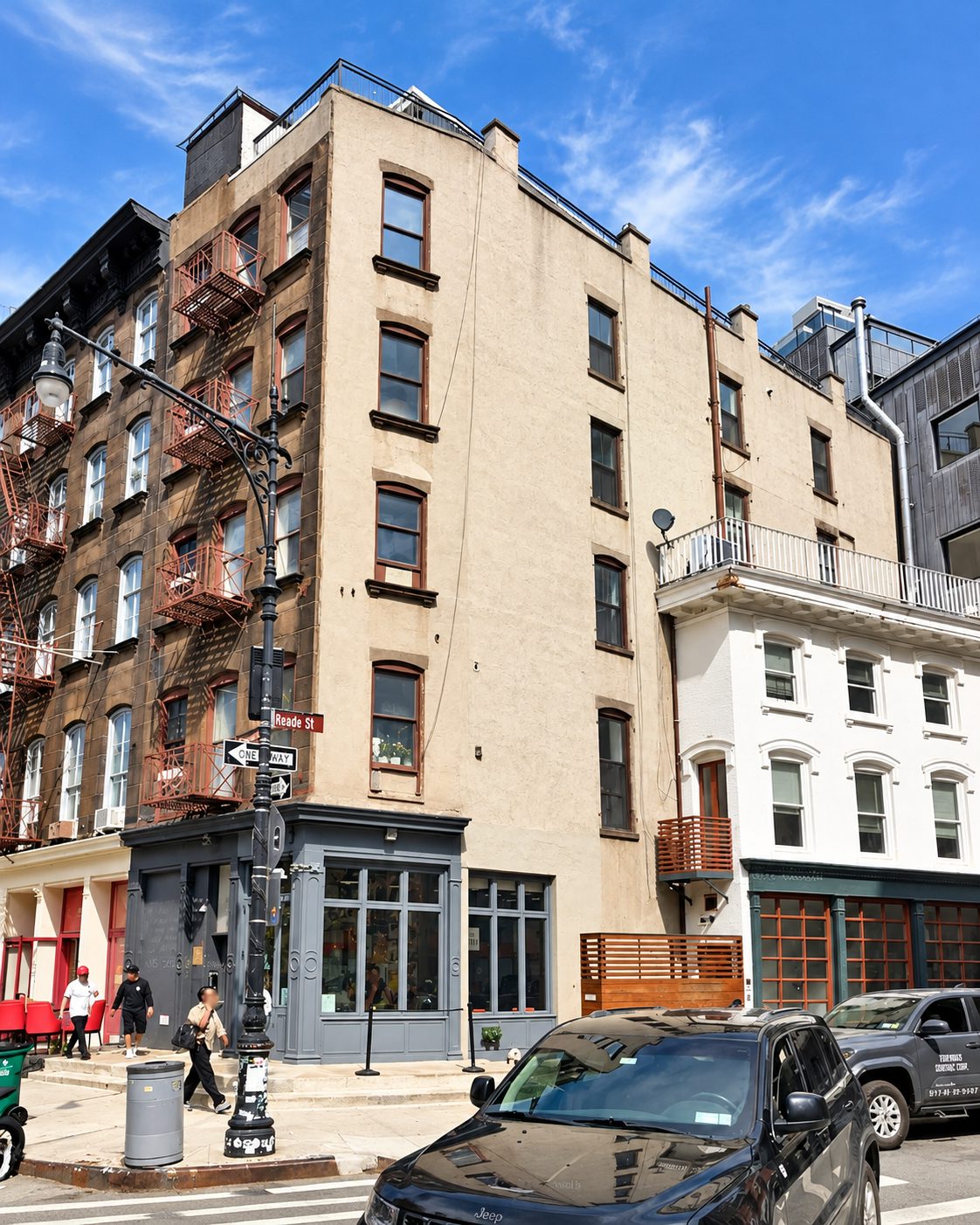 Corner view of 315 Greenwich Street, a five story building with a tan stucco side elevation and brown framed windows, beside a brown building with red fire escapes and a white painted section at the right