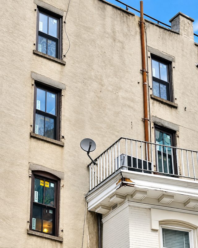 Detail of the upper side elevation with new black framed double hung windows, a copper colored drain pipe and a balcony with a satellite dish