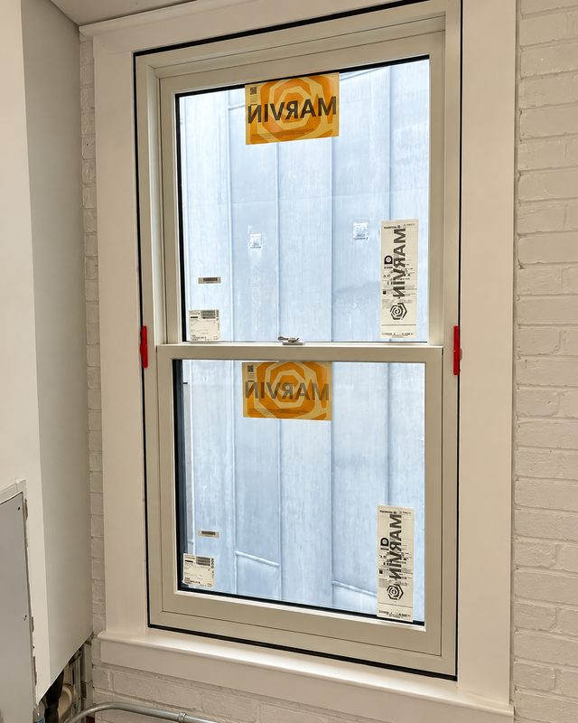 Inside view of a new double hung window with orange Marvin labels, set in a white painted brick opening
