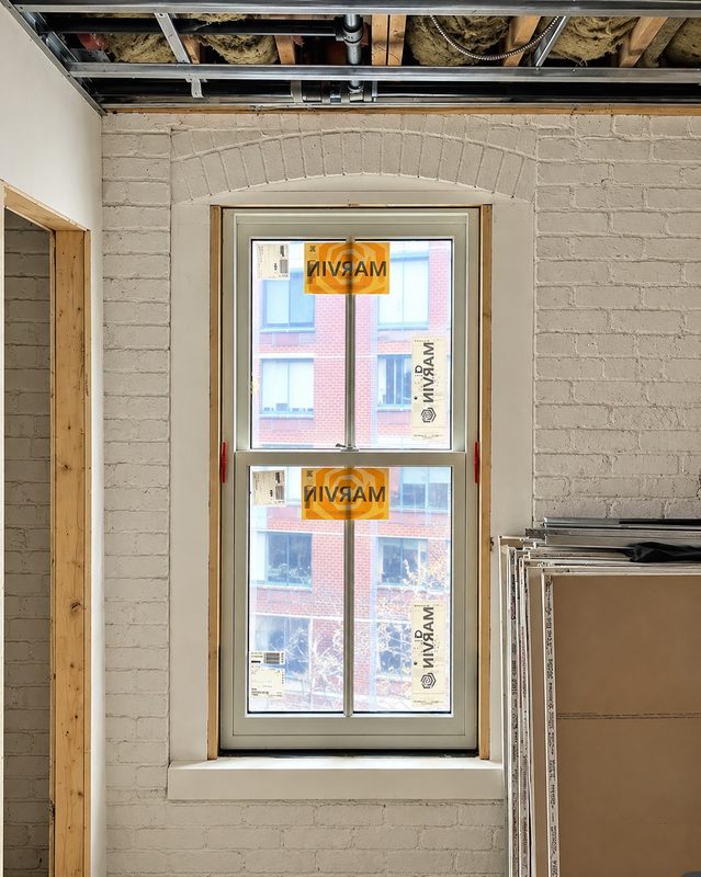 Inside view of a new double hung window in a painted brick opening with a brick arch above and an unfinished ceiling